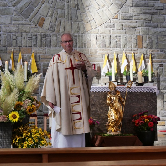 Der Pfarrer predigt im Gottesdienst. Er ist dazu nach vorn vor den Altar zur Figur des Kirchenpatrons gekommen.