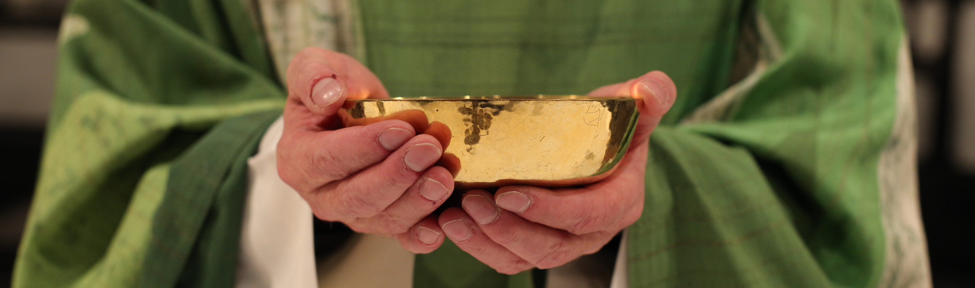 Ein Priester hält eine Patene in der Hand.